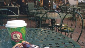 A table with a pastry and a coffee cup, surrounded by metal chairs and tables in an outdoor setting.