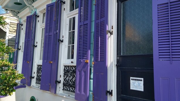 A building with white walls and teal trim, featuring purple shutters on the windows and doors.