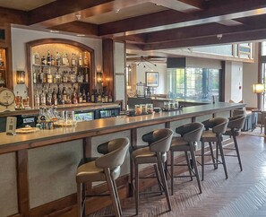 Eine Bar mit einer langen Theke, mehreren Hockstühlen und einer Auswahl an Flaschen und Gläsern.