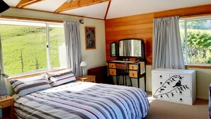 Une chambre à coucher comprenant un lit, un bureau, une commode et une grande fenêtre avec des rideaux.