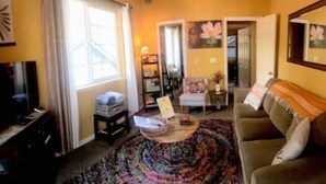 A living room with a sofa, a coffee table, and a television. There is a window with curtains, a door leading to another room, and a mirror on the wall. - HAKUNA MATATA  (South Lake Tahoe)
