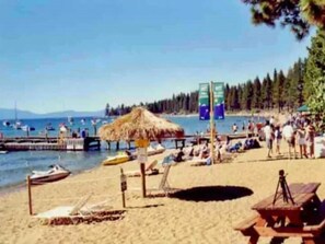 Una playa con un quiosco de paja, una mesa de madera y un muelle con barcos.