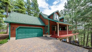 A log cabin with a green garage, a covered porch, and a brick driveway. - The Gracia Inn-Luxury Cabin amidst Ponderosa Pines (Flagstaff)
