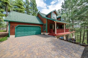 A log cabin with a green garage, a covered porch, and a brick driveway.
