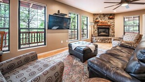 A spacious living room with a fireplace, large windows, a ceiling fan, and a mounted TV. - The Gracia Inn-Luxury Cabin amidst Ponderosa Pines (Flagstaff)