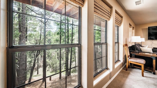 A room with large windows offering a forest view, a desk with a chair, and a television on the wall. - The Gracia Inn-Luxury Cabin amidst Ponderosa Pines (Flagstaff)