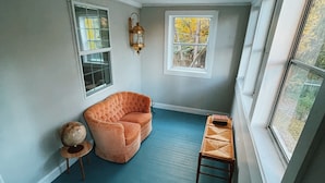 A room with a blue floor, a curved orange chair, a small round table, and two windows. - Quiet renovated cottage by Seabreeze (Rochester)