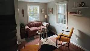 A living room with a sofa, armchair, and a small table with candles. There is a staircase leading to another level. - Quiet renovated cottage by Seabreeze (Rochester)