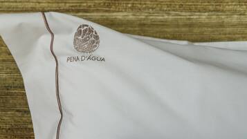 A white pillow with "PENA D'ÁGUA" embroidered on it, placed on a wooden surface.