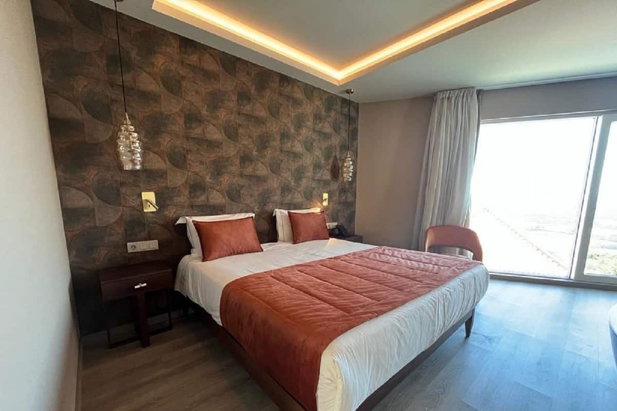 Ein modernes Schlafzimmer mit einem großen Bett, einer Steinsäule und Blick ins Freie.