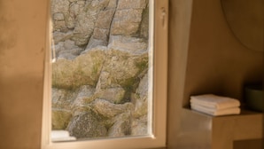 A bathroom with a stone wall view, a bench with a towel, and a round mirror. - Pena D'Água Boutique Hotel & Villas  (Covilhã)
