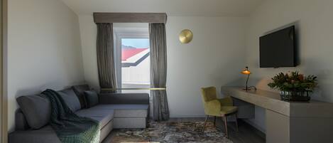 A modern room with a grey sofa, a yellow chair, a desk with a lamp, and a TV mounted on the wall.