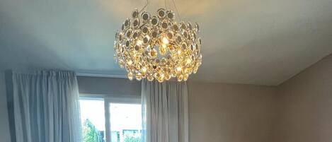 A modern living room with a brown sofa, a dining table with chairs, and a decorative chandelier.