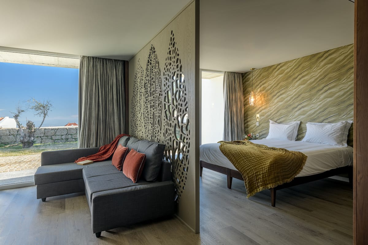 Ein modernes Schlafzimmer mit Bett, Sofa und Blick ins Freie.