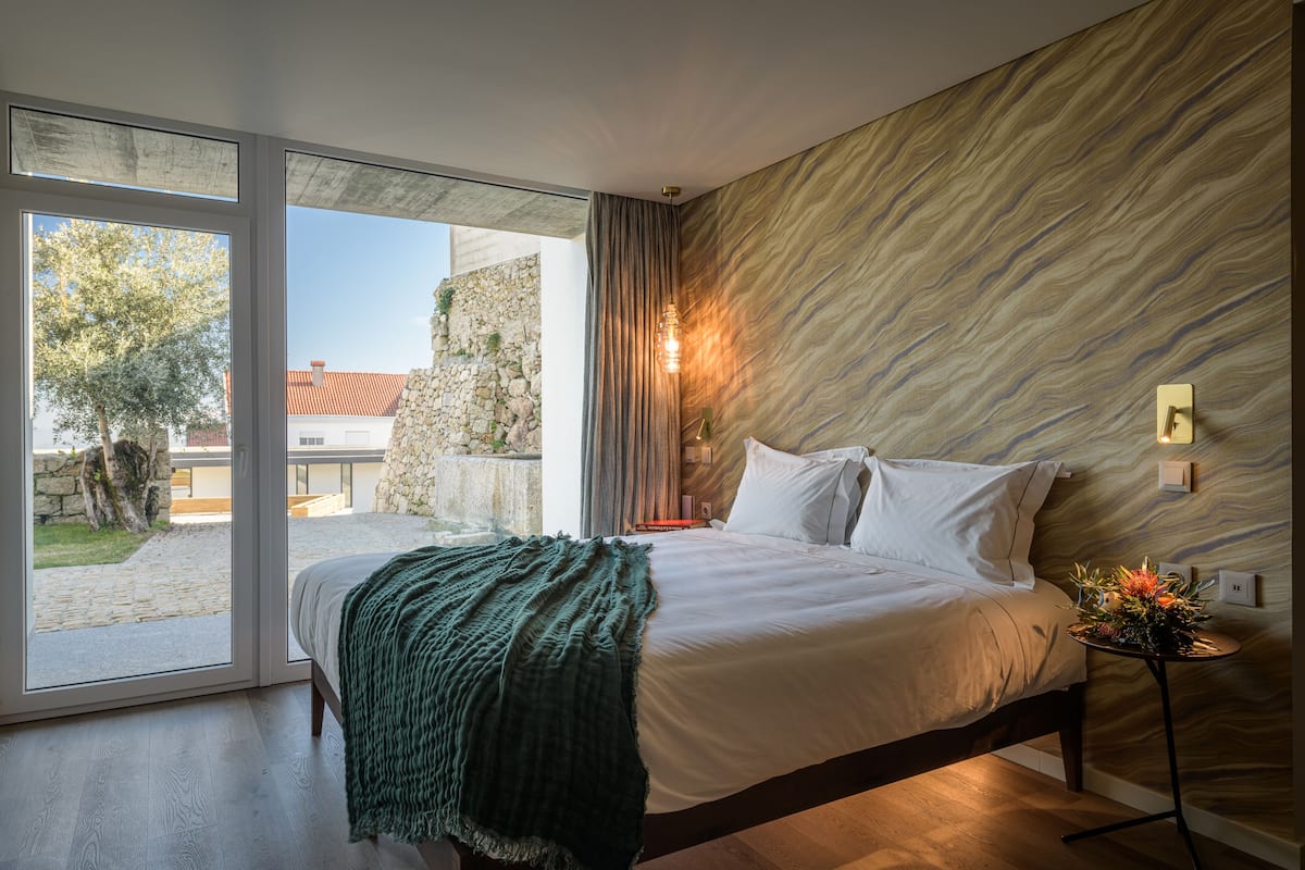 Ein modernes Schlafzimmer mit einem großen Bett, Blick durch eine Schiebetür und einer Steinwand.