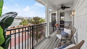 Ein Balkon mit Korbmöbeln, einem Deckenventilator und Blick auf die Straße.