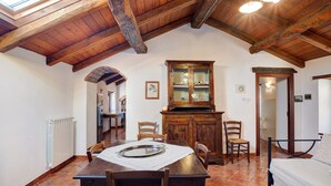 A dining area with a wooden table, chairs, a cabinet, and a bed in a room with a sloped ceiling and tiled floor.