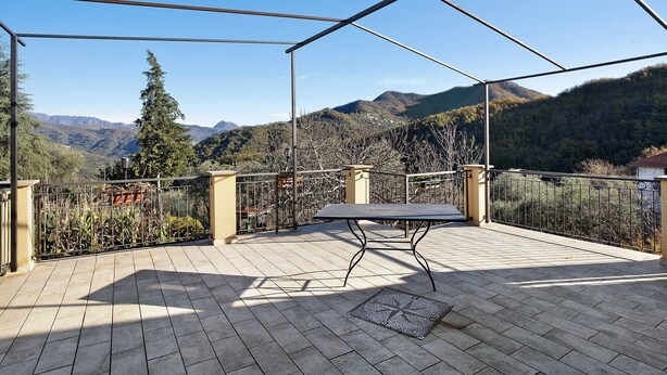 A covered outdoor area with a table and chairs, a metal railing, and a view of mountains.