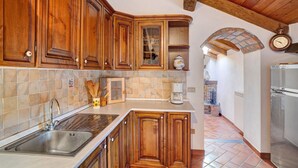 A kitchen with wooden cabinets, a stainless steel sink, a coffee maker, and a clock on the wall.