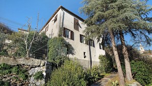 A two-story house with a stone pathway leading to the entrance, surrounded by greenery and trees.
