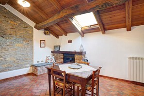 Ein Essbereich mit Steinwand, Holzbalkendecke, Kamin und Fliesenboden.