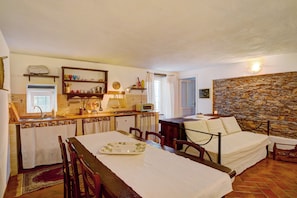 Una habitación compacta con mesa de comedor, cama, zona de cocina y pared de piedra.