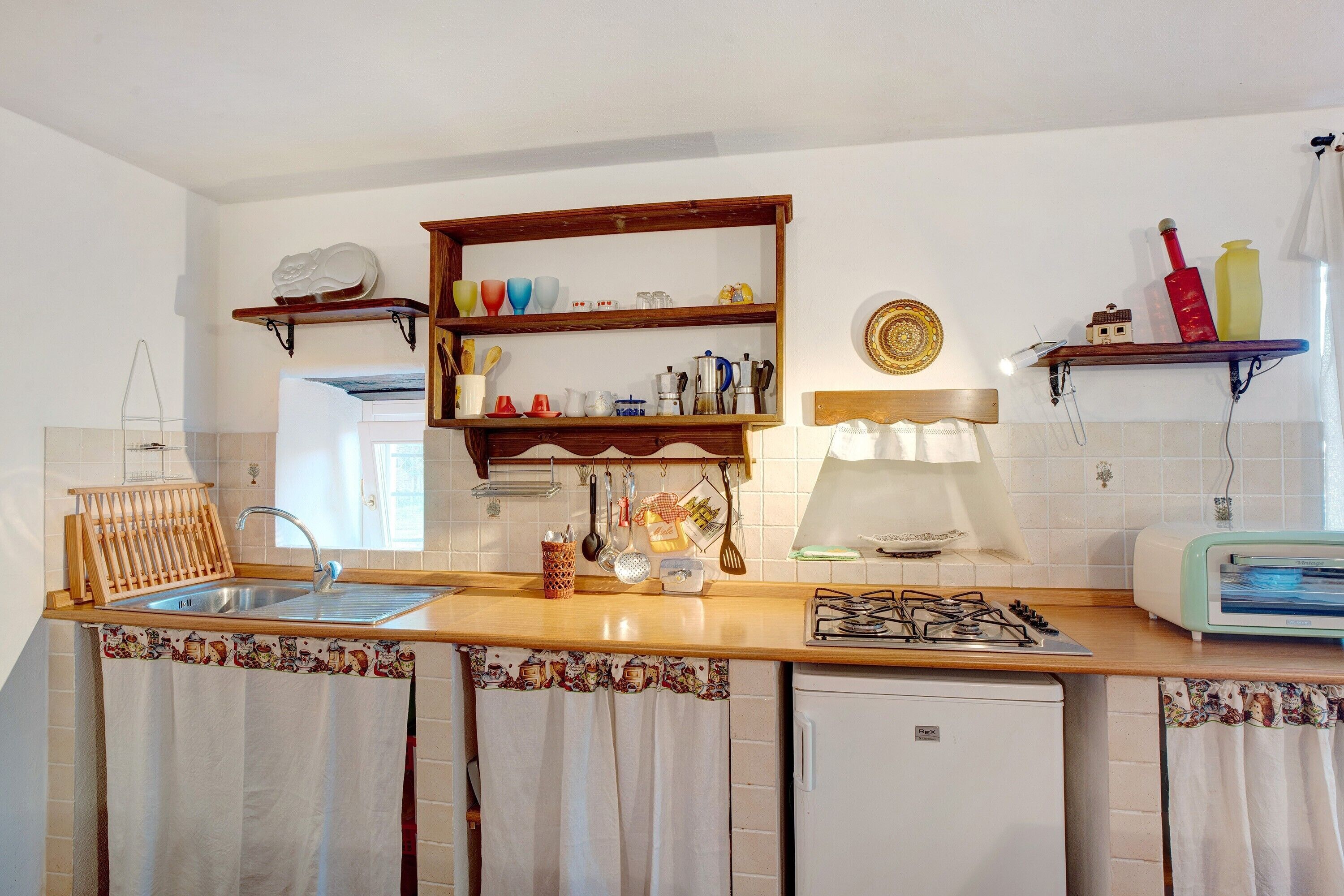 Una cucina con un piano di lavoro in legno, un fornello a gas, un frigorifero bianco e mensole piene di utensili da cucina.