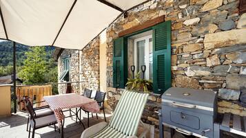 A stone building with a balcony, outdoor seating, and a grill.