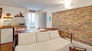 Habitació acollidora amb paret de pedra, llit de fusta, petita cuina i vistes cap a l'exterior.
