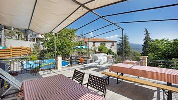 An outdoor patio with tables and chairs, a pool, and a view of the surrounding landscape.