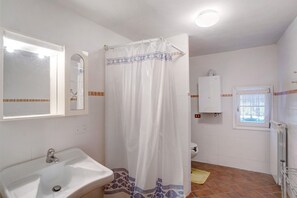 Une salle de bain avec un lavabo blanc, un rideau de douche, un miroir, des toilettes et une fenêtre.