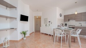 Eine moderne Küche mit weißen Schränken, einem Esstisch mit Stühlen, einem an der Wand montierten Fernseher und einem Blumentopf.