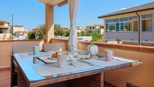 Ein Balkon mit Frühstückstisch, mit Croissants und Kaffeetassen, mit Blick auf ein Wohngebiet.