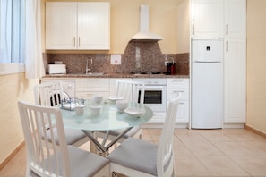 A modern kitchen with white cabinets, a glass table, and a white refrigerator.