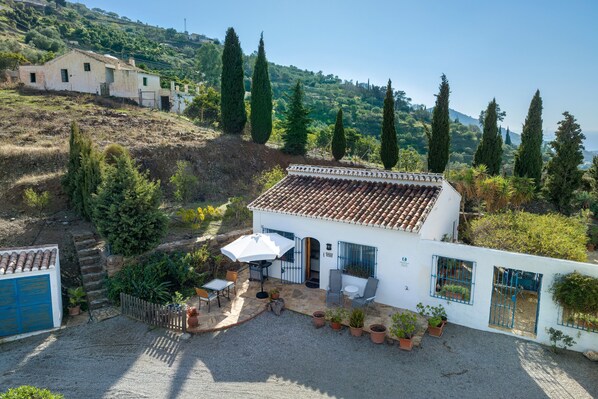 Un bâtiment blanc avec un toit en tuiles, une terrasse dotée de mobilier d’extérieur et une vue sur un paysage vallonné.