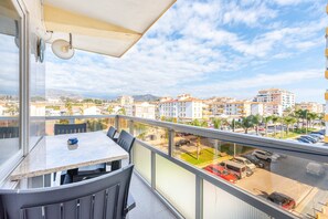 A balcony with a table and chairs, a view of a cityscape with buildings and a parking lot.