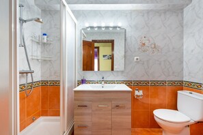 Un baño con ducha, lavabo, inodoro y espejo.