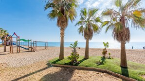 Une plage bordée de palmiers, avec un filet de volley-ball et une aire de jeux.