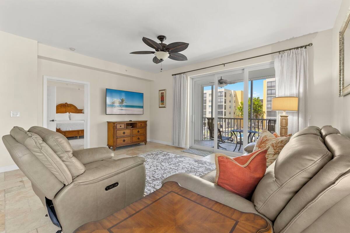 A living room with a reclining sofa, a ceiling fan, a view of the outside balcony, and a painting on the wall.