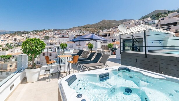 Een dakterras met een jacuzzi, lounge stoelen en een tafel met stoelen.