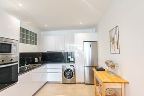 A compact kitchen with a washing machine, a refrigerator, and a microwave. - Modern Apartment in Cómpeta I with Mountain View, Wi-Fi & Terrace (Cómpeta)