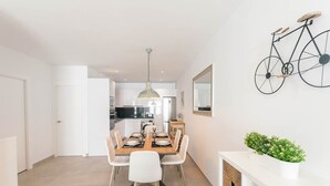 Een moderne keuken met witte kasten, een eethoek met een houten tafel en witte stoelen, en een fiets aan de wand.