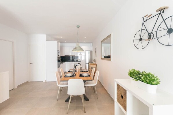 A modern kitchen with white cabinets, a dining area with a wooden table and white chairs, and a bicycle mounted on the wall. - Modern apartment in Cómpeta with shared pool and jacuzzi (Cómpeta)