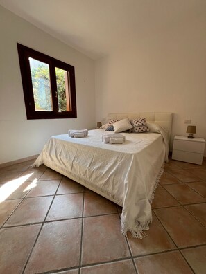 A bedroom with a bed, pillows, a nightstand, and a window.
