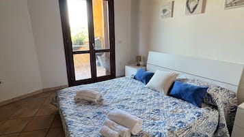 Un dormitori amb un llit, una tauleta de nit, una làmpada i una porta que dona a zona exterior.