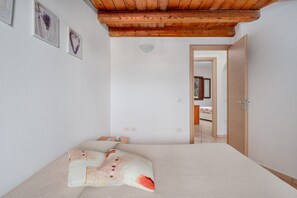 A bedroom with a bed, a wooden ceiling, and a door leading to another room.