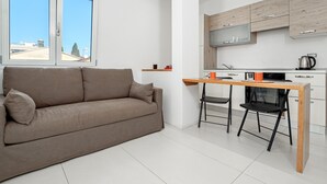 Eine moderne Wohnung mit Sofa, Esstisch, Stühlen, einer Küchenzeile und Blick durch große Fenster.