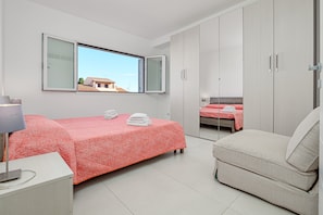 A bedroom with a bed, a nightstand, a chair, a wardrobe, and a window with a view of buildings.