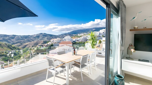 A balcony with a table and chairs, a TV, and a view of a mountainous landscape. - Stunning Apartment in Cómpeta (Cómpeta)