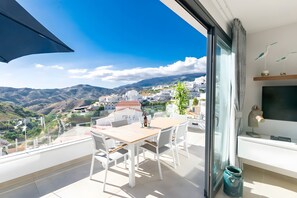 A balcony with a table and chairs, a TV, and a view of a mountainous landscape. - Stunning Apartment in Cómpeta with Private BBQ, Shared Pool & Jacuzzi (Cómpeta)